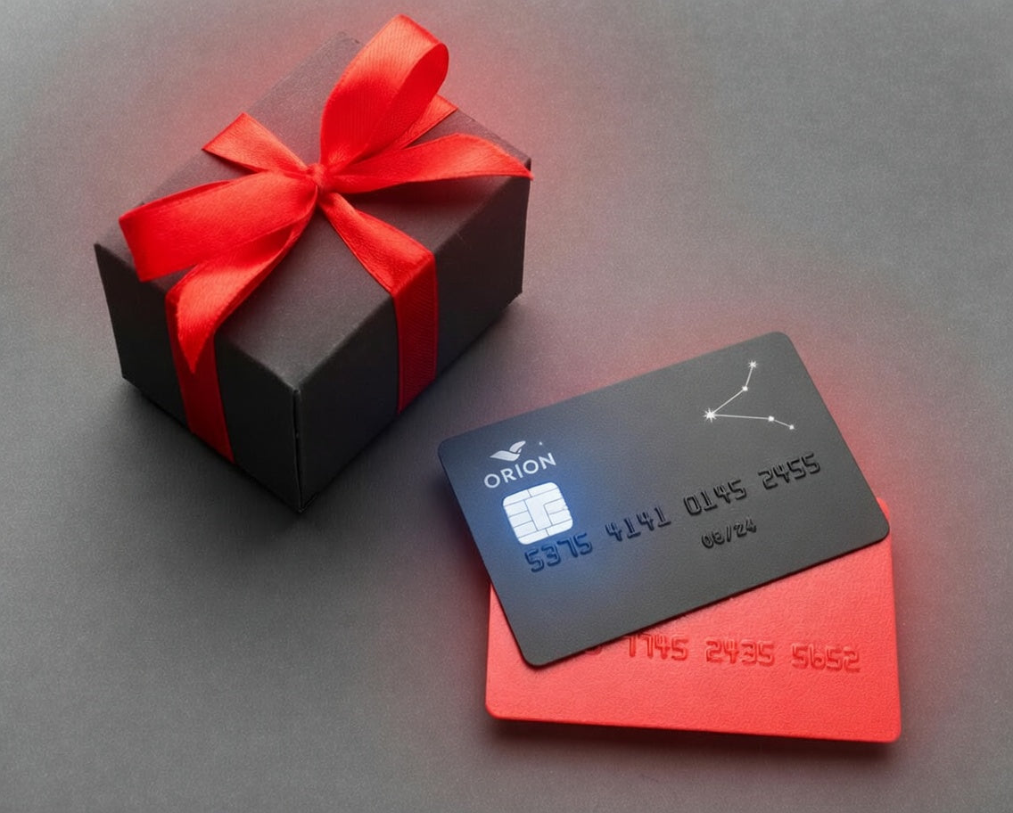 Black gift box with red ribbon and Orion gift card on a gray surface